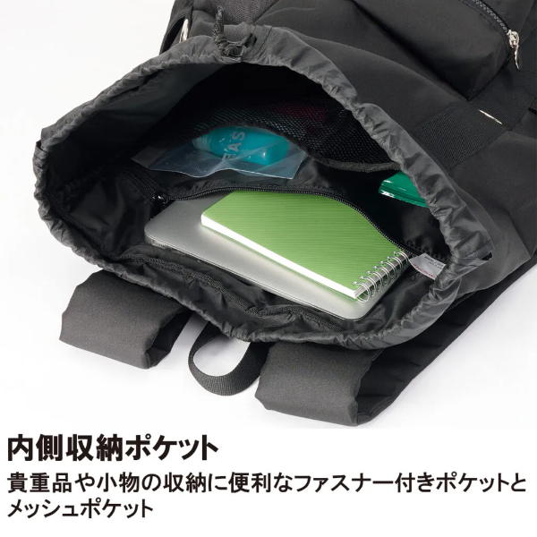 Backpack opened to show internal storage with a zipper pocket, mesh pocket, and items including a green spiral notebook and a silver laptop inside.
