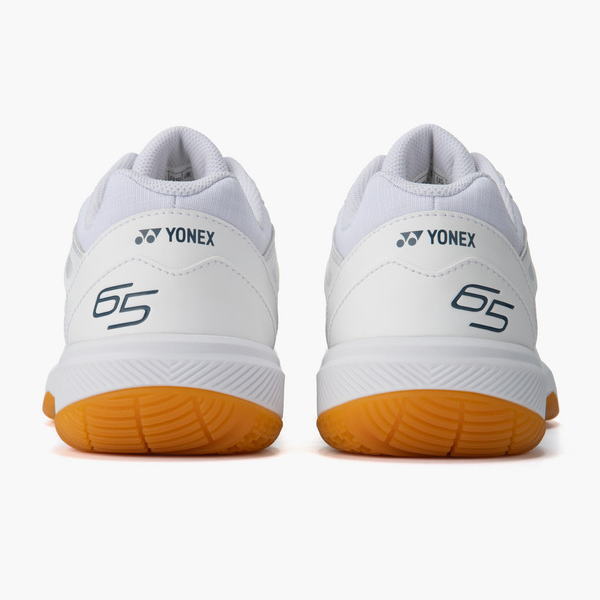 Pair of white Yonex sneakers seen from the back with orange rubber outsoles.