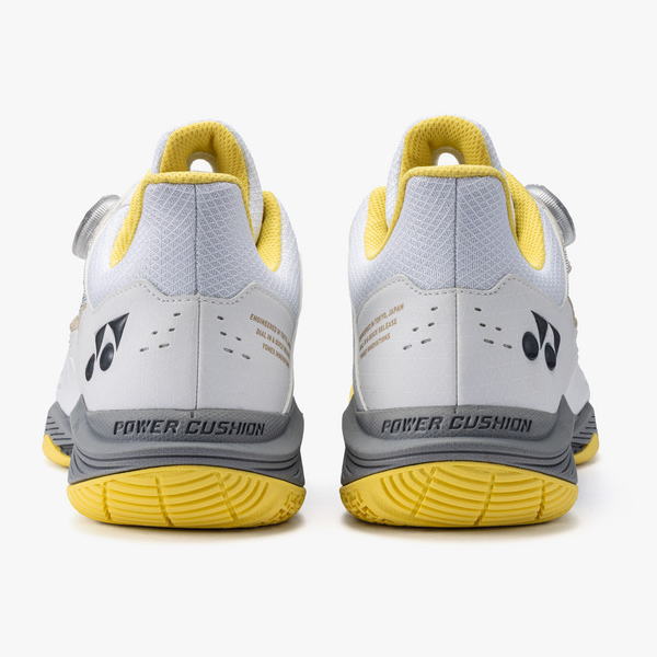 Pair of white and gray athletic sneakers with yellow lining, seen from the back showing the Power Cushion branding on the heel and a black logo on each shoe.