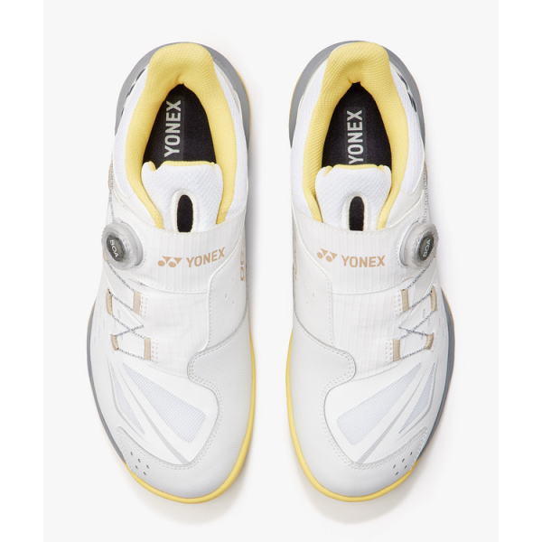 Top-down view of white Yonex athletic shoes with yellow lining.