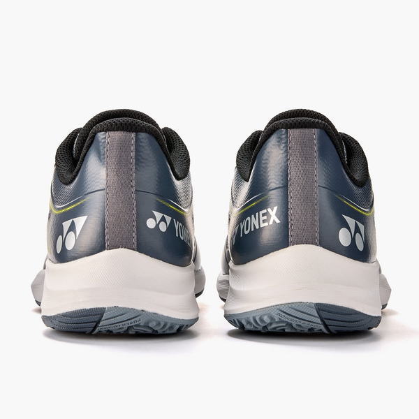 Rear view of two navy Yonex athletic shoes with white soles, showing Yonex logo on heels and neon accents.