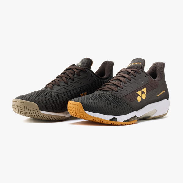 Pair of Yonex athletic shoes in black and brown with orange outsoles and textured mesh uppers.
