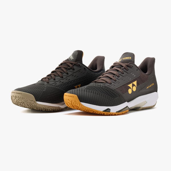 Pair of Yonex badminton shoes in black-brown with yellow logo, shown from a side-front angle on a white background.