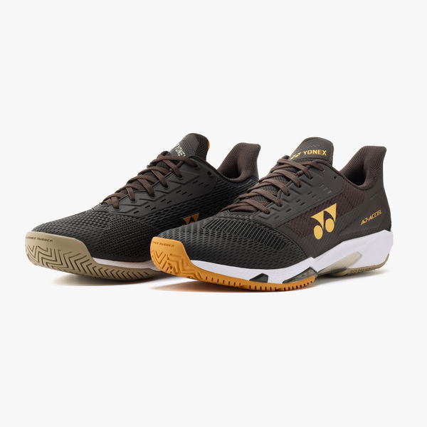 Pair of black Yonex athletic shoes with brown laces and yellow logo, orange outsole, designed for court play.