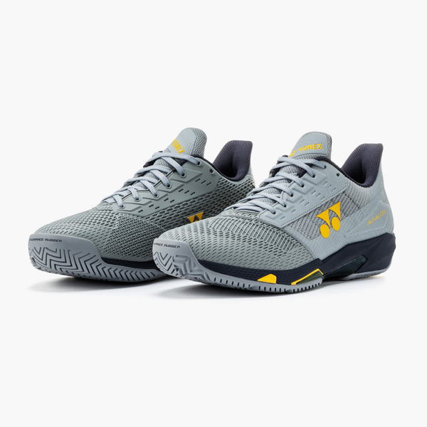 Pair of grey athletic shoes with mesh uppers and yellow accents, angled to show sides and soles.