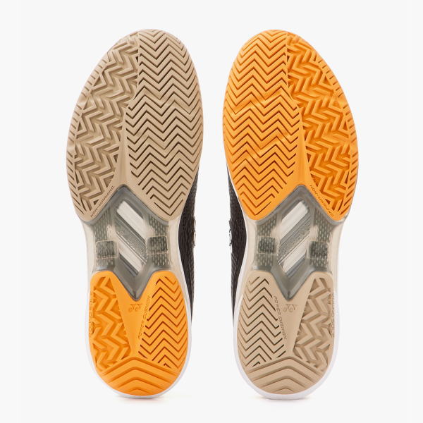 Bottom view of two running shoe soles, left tan and right orange, showing chevron tread and midfoot cushioning.