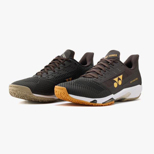 Pair of black-brown Yonex badminton shoes with orange outsole and laced closure, shown from a side angle on a white background.