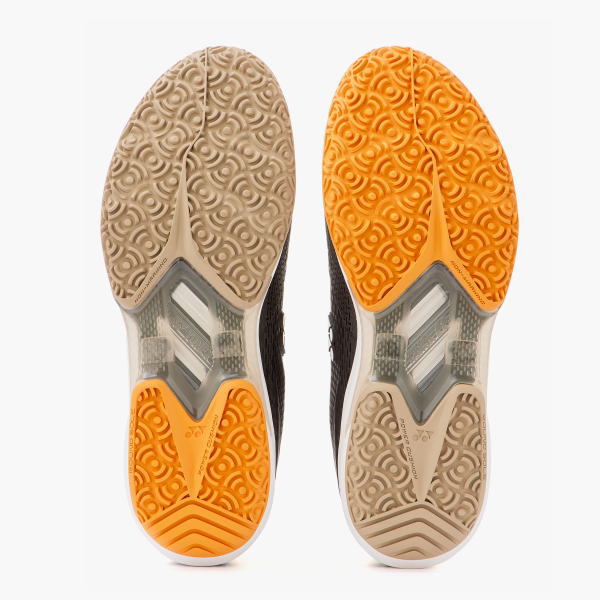 Bottom view of two running shoes side by side, left beige sole and right orange sole with circular tread patterns.