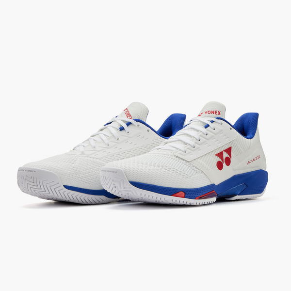 White Yonex tennis shoes with blue lining and accents, shown from a side angle for court performance.