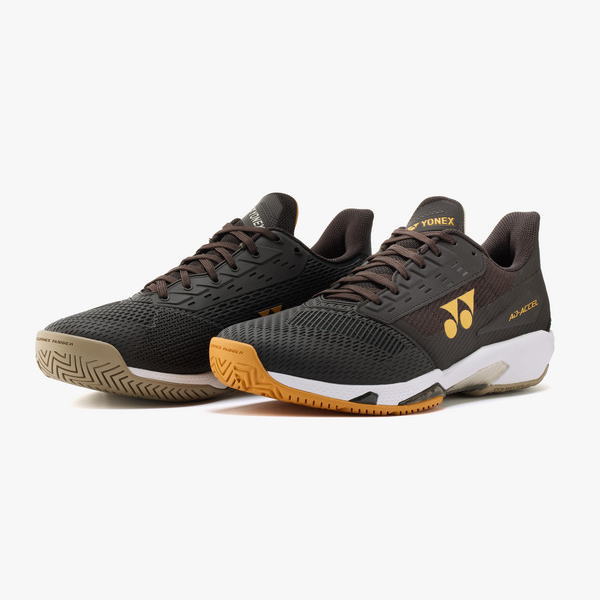 Black Yonex athletic shoes with orange accents, low-cut badminton sneakers for court use; breathable mesh and grippy outsole visible.