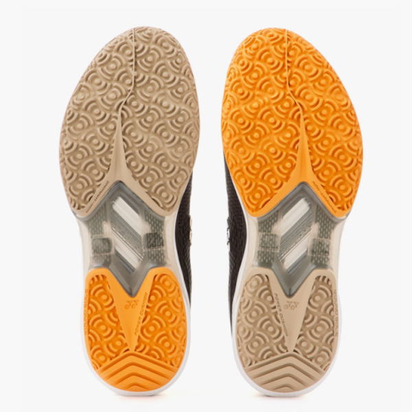 Outsoles of two running shoes side by side, left in beige and right in orange, showing tread patterns and midfoot plates for grip and stability.